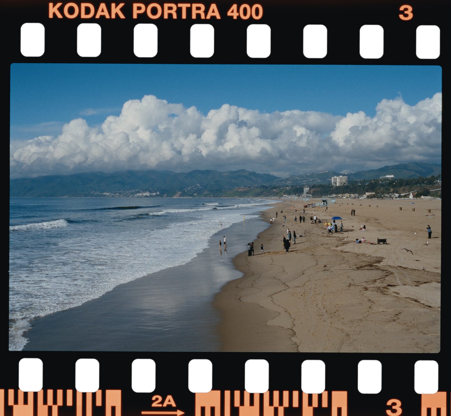 A long beach under cumulus, Kodak Portra 400 on a 135 strip with its edge print and frame number.